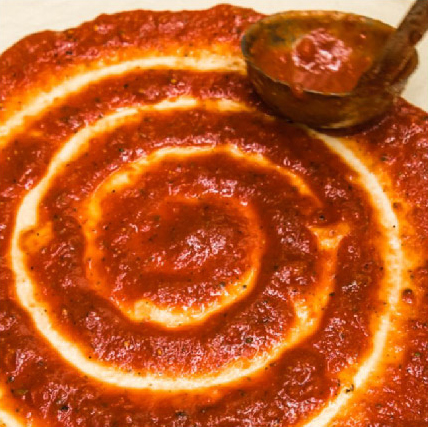 Sauce being spread in a spiral on a pizza.